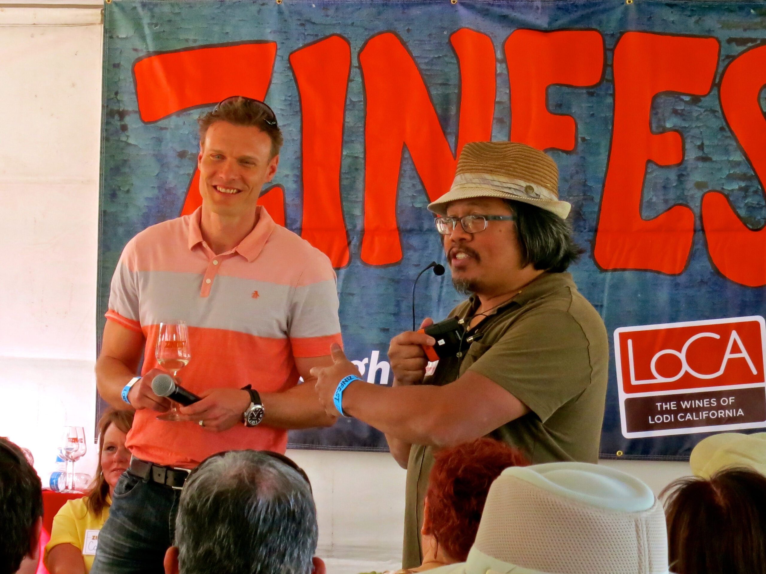 Two men speaking at a Lodi Winegrape Commission event with a banner in the background.