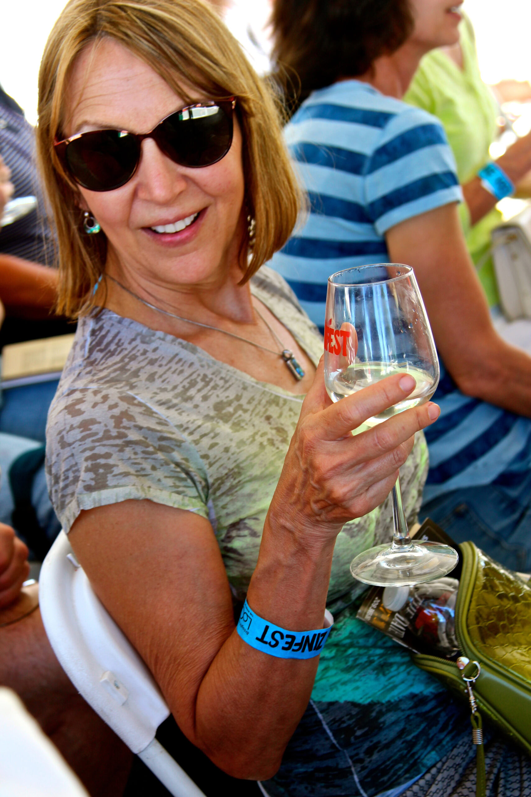 Woman enjoying wine at Lodi Winegrape Commission event, smiling with sunglasses, holding a glass of white wine.