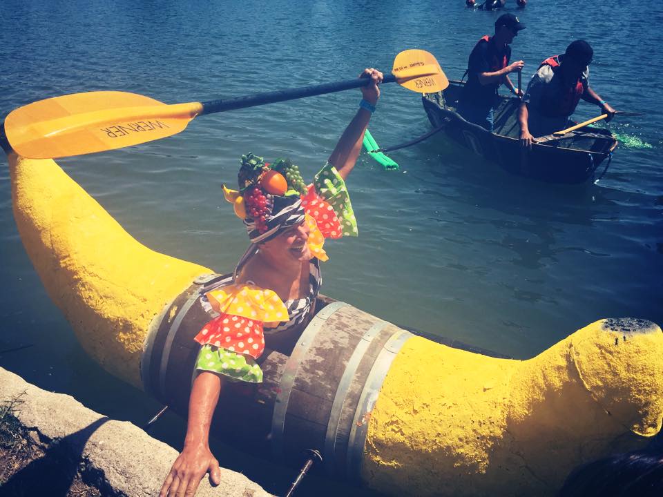Person in colorful costume paddling a yellow boat on water with others in boats nearby.