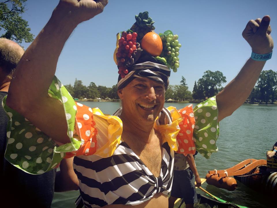 Person celebrating outdoors with fruit-themed costume near water, representing Lodi Winegrape Commission.