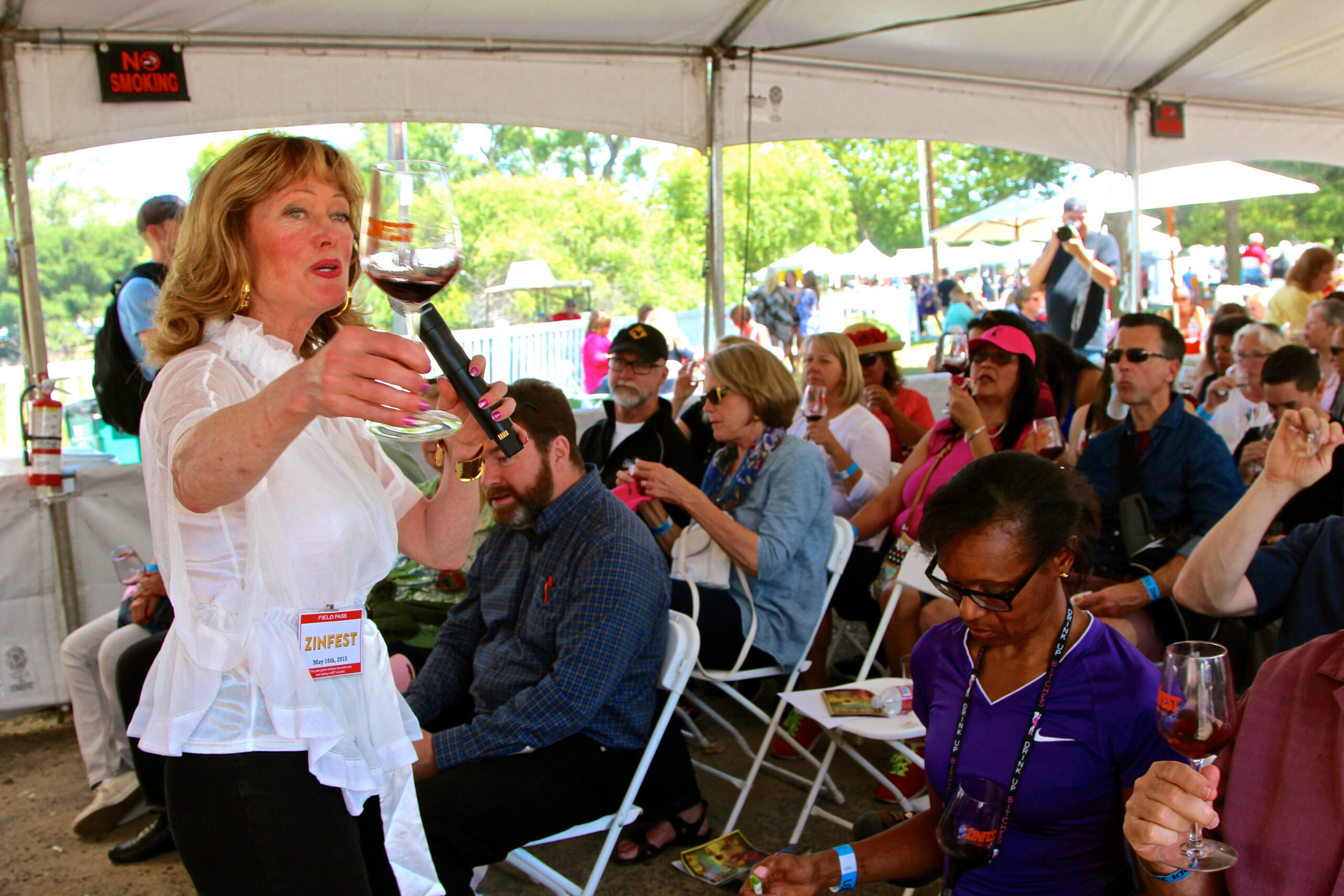 Woman tasting wine at Lodi Winegrape Commission event with audience in a tent.