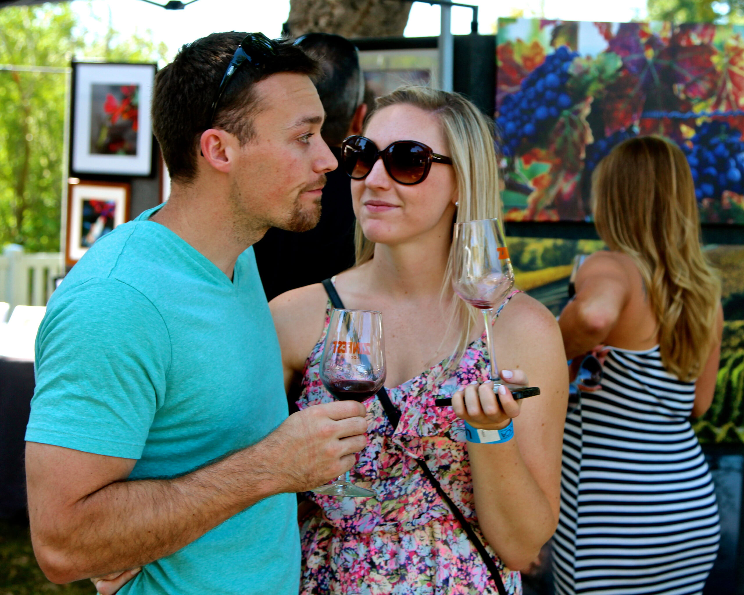 Couple enjoying wine tasting at Lodi Winegrape Commission event with art displays in background.