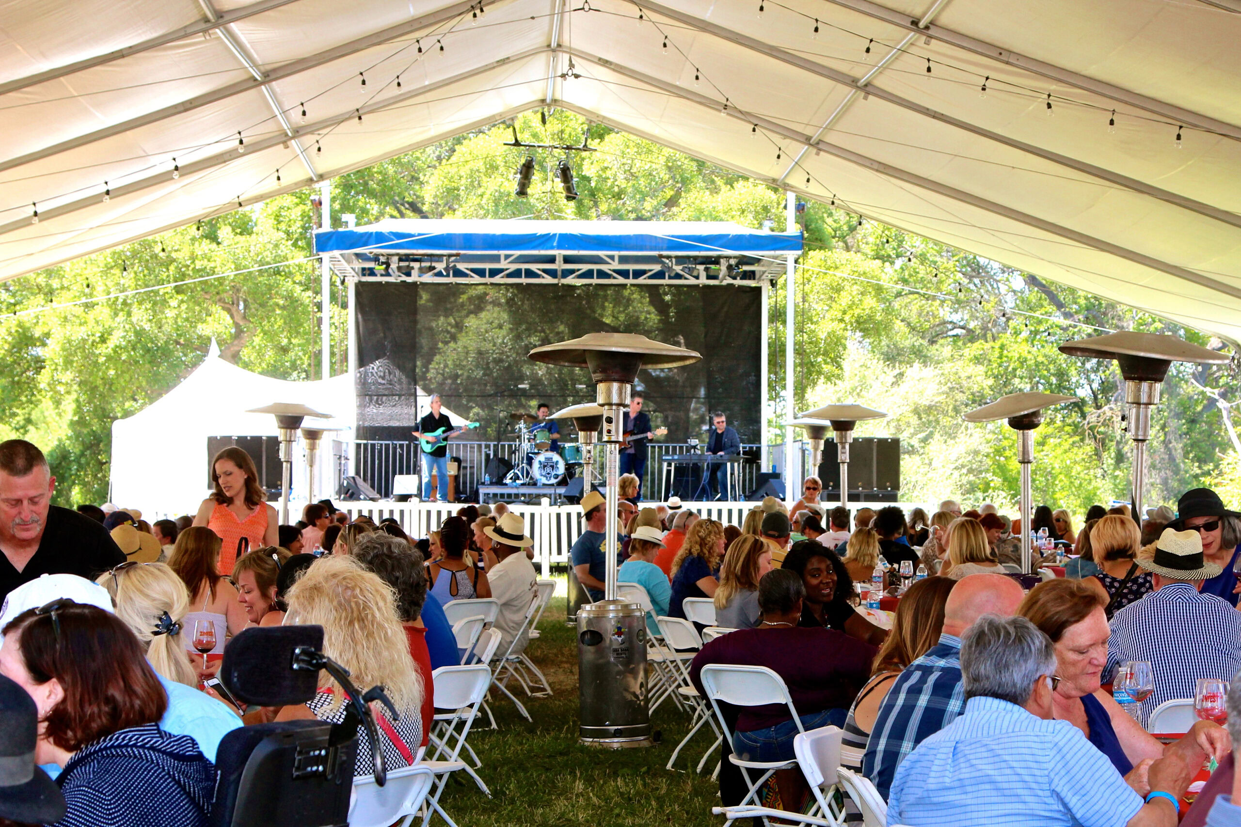 Crowd enjoying outdoor event with live band and wine under a large tent in Lodi, California.