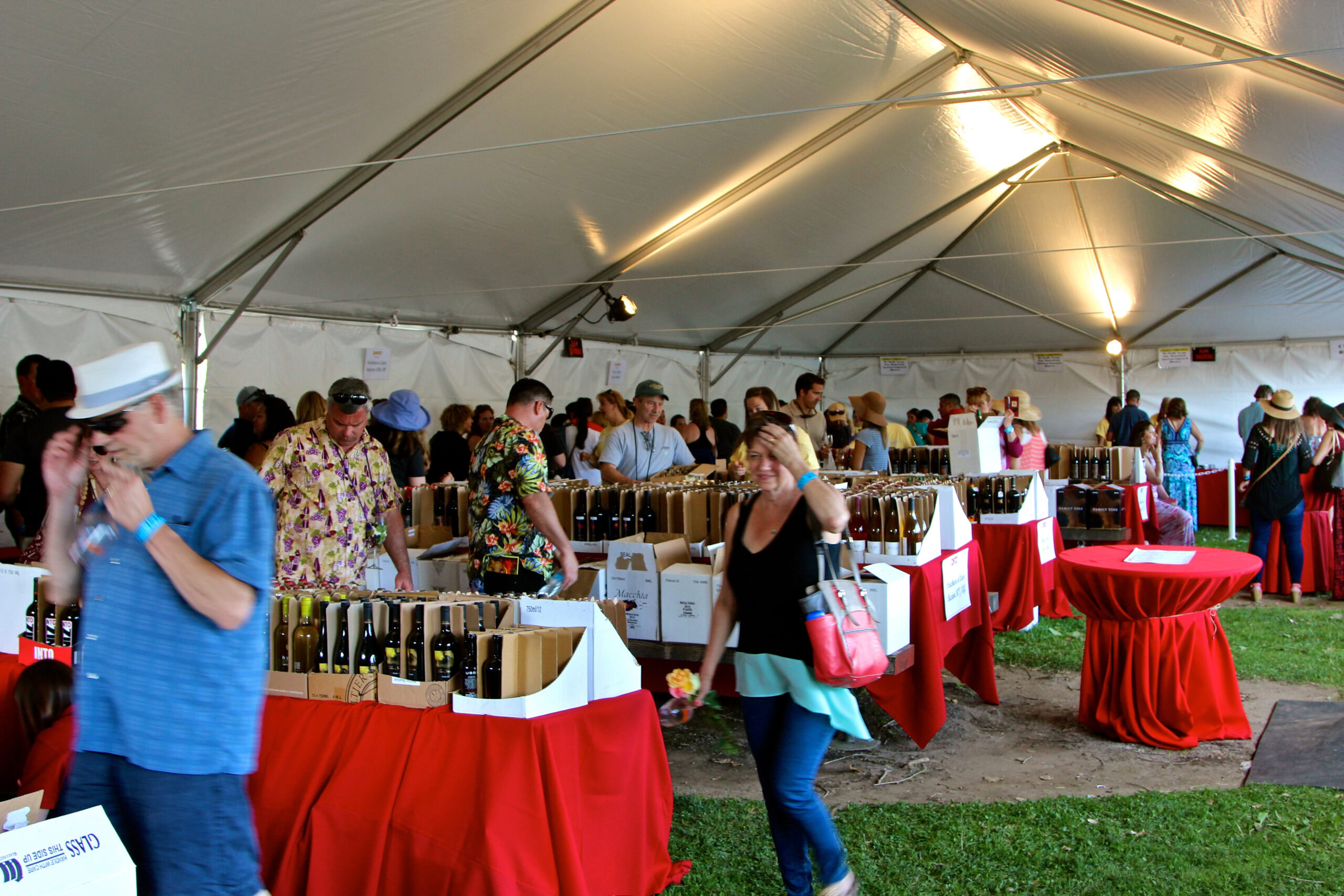 Visitors at Lodi Winegrape Commission tasting event under a large white tent with wine bottles on display.