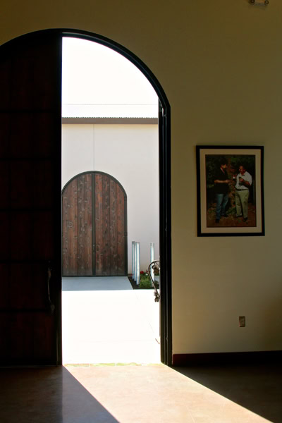 Interior view of a building with an open door leading outside, framed by a large arched doorway, with a photo on the wall.