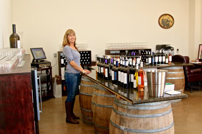 Woman sampling wine at Lodi Winegrape Commission tasting room with wine bottles and barrels.