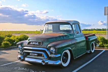 Old GMC pickup truck parked in a vineyard with lush green fields and a blue sky in Lodi, California.