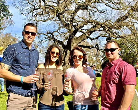 Group of four people enjoying wine tasting outdoors with a large tree in the background.