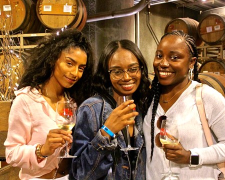 Three women smiling and tasting wine at Lodi Winegrape Commission event in a winery setting.