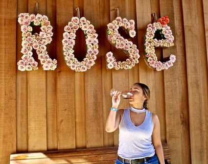 Woman drinking wine in front of rose flower letters spelling 'ROSE' at Lodi Winegrape Commission event.