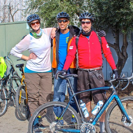 Three cyclists with helmets and backpacks posing with bikes outdoors at Lodi Winegrape Commission event.