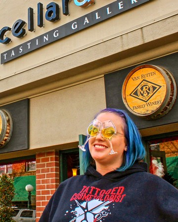 Woman with blue hair and sunglasses smiling outside Van Ruiten Family Winery tasting room.
