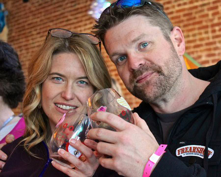 Two people enjoying wine at a Lodi Winegrape Commission event, smiling and clinking glasses.