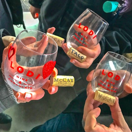 Group of people holding Lodi Winegrape Commission branded wine glasses with wine and corks.
