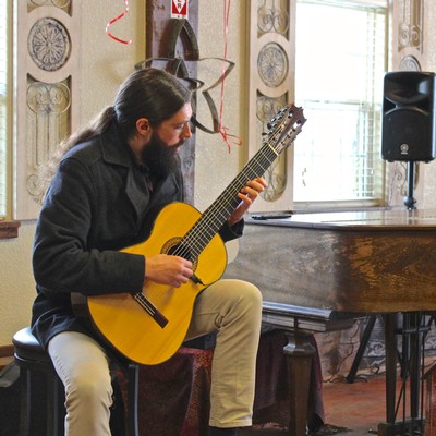 Man playing acoustic guitar at Lodi Winegrape Commission event, indoor setting with ornate decor and natural light.