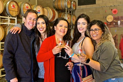 Group of five diverse people smiling and holding wine glasses at a wine tasting event.