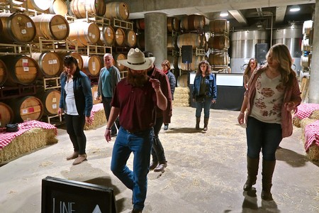 Group touring a winery with wine barrels and staff, exploring Lodi's wine production and grape varieties.