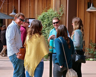 Group of people enjoying a wine tasting event outdoors, smiling and engaging in conversation.