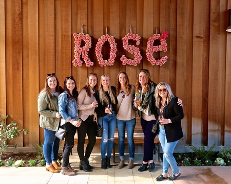 Group of women celebrating at Lodi Winegrape Commission with rose-themed decor in the background.