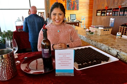 Smiling woman at Lodi wine tasting event with wine bottle and chocolates on bar.