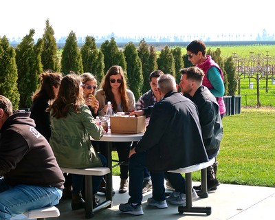 Group of people enjoying outdoor wine tasting event at Lodi Winegrape Commission vineyard.