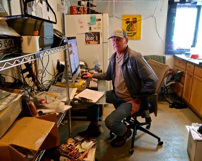 Man working at desk in wine industry office with computer and wine-related decor.