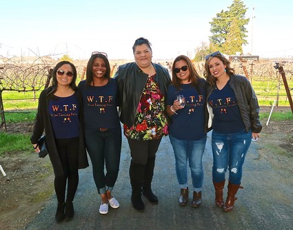 Group of five women standing outdoors in a vineyard, smiling, with the Lodi Winegrape Commission logo on their shirts.