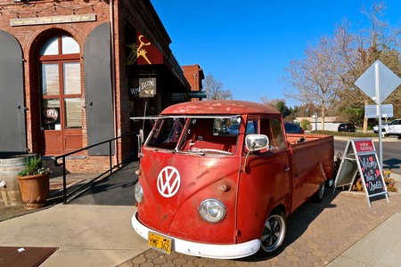 Red vintage Volkswagen van parked outside a wine shop in Lodi, California, with clear blue sky and trees in the background.