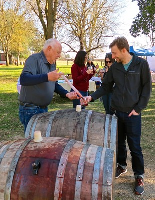 People enjoying wine tasting outdoors at a Lodi wine event with barrels and trees in the background.