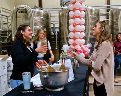 Two women enjoying wine tasting at a Lodi wine event with wine tanks in the background.
