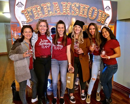 Group of women enjoying wine tasting at Freakshow event, smiling and holding glasses, in front of a colorful banner.