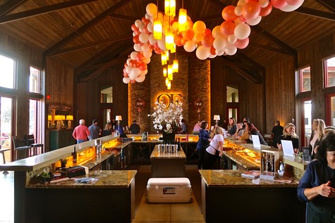 Elegant event space with high wooden ceilings, hanging lights, and balloon decorations, hosting a social gathering.