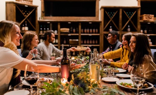 Group of people enjoying wine tasting at a wine bar with wine bottles and glasses on the table.
