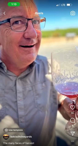 Close-up of a smiling man holding a glass of red wine outdoors during harvest season.
