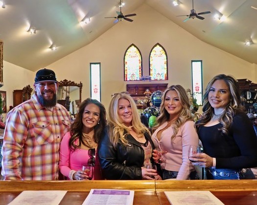 Group of five people at a wine tasting event inside a church with stained glass windows.