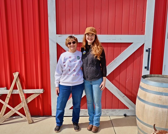 Two women standing in front of a red barn at a Lodi wine event, smiling and enjoying the day.