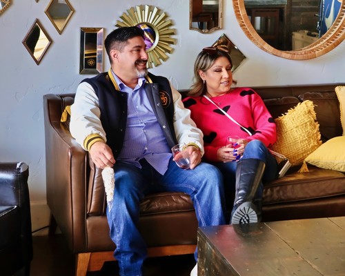 Two people enjoying a social event, with wine glasses, in a cozy, stylish setting.