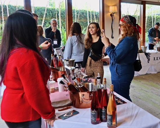 People enjoying wine tasting at Lodi Winegrape Commission event with wine bottles and glasses on display.