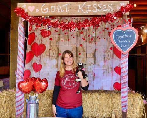 Woman holding a puppy at a Valentine's Day themed event with hearts and decorations.