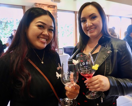 Two women smiling and holding glasses of red wine at a Lodi Winegrape Commission event.