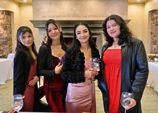 Group of women at a wine tasting event, holding glasses of wine, smiling, in a cozy indoor setting.