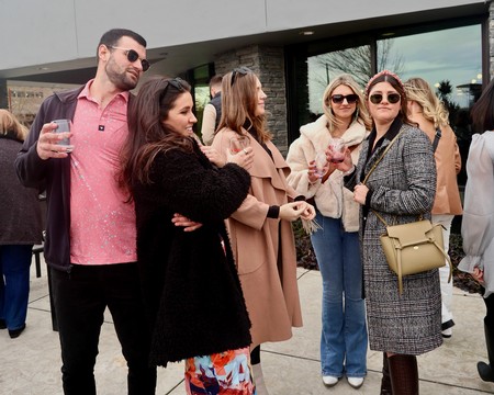 Group of people enjoying a wine tasting event outdoors, engaging in conversation and holding wine glasses.