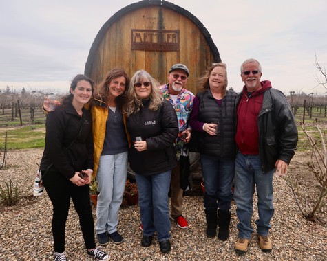 Group of people at Lodi Winegrape Commission event in a vineyard with a large wine barrel in the background.