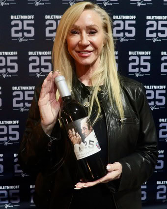 Woman holding a bottle of wine at Lodi Winegrape Commission event with backdrop.
