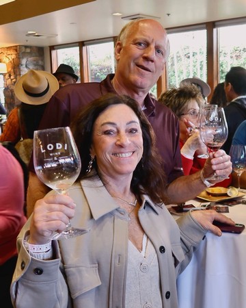 Two people enjoying wine tasting at a Lodi Winegrape Commission event, smiling and holding wine glasses.