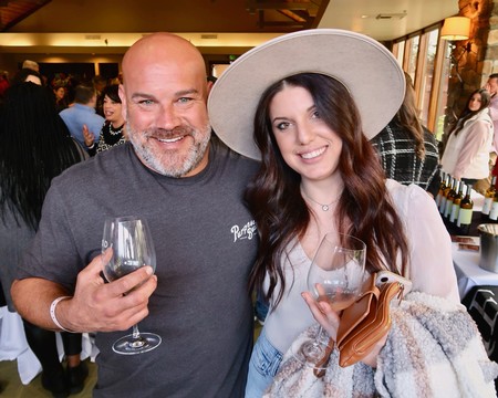 Two smiling people enjoying wine at a Lodi Winegrape Commission event, with a lively crowd in the background.