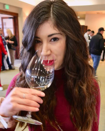 Young woman tasting wine at Lodi Winegrape Commission event, holding a glass of white wine.