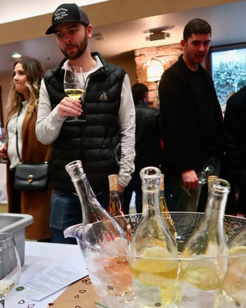People enjoying wine tasting at a Lodi Winegrape Commission event with wine bottles and glasses on display.