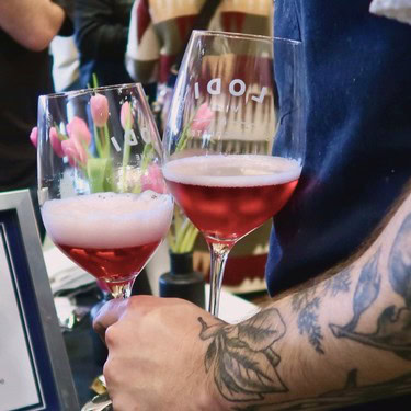 Two glasses of red wine held by a person with tattoos at a wine tasting event.
