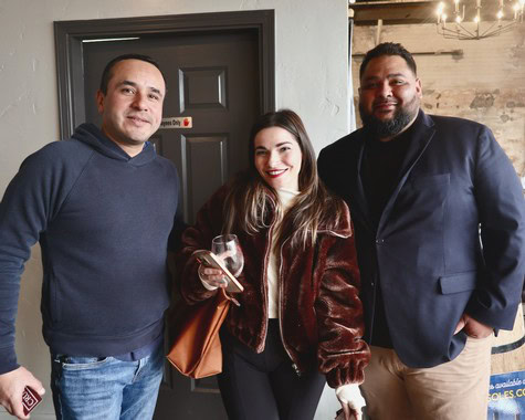 Group of three diverse people at Lodi Winegrape Commission event, smiling, holding wine glass, indoor setting.